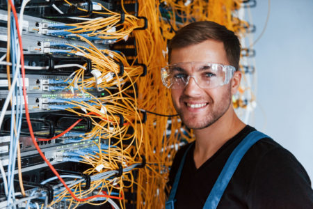 Young man in protective glasses works with internet equipment and wires in server room Young man in protective glasses works with internet equipment and wires in server room.